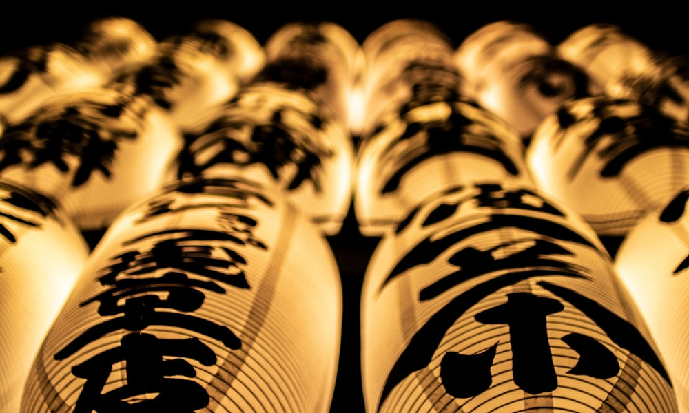 Reihen beleuchteter japanischer Chōchin-Papierlaternen mit schwarzen Kanji in einer Straße