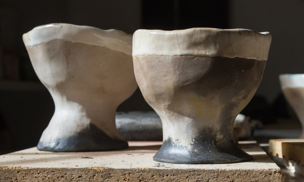 Zwei japanische Raku-Teeschalen (Chawan) mit handgeformten Formen und Glasurtönen von dunkel bis hell, auf einer Werkstattfläche