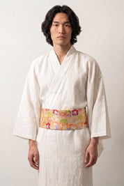 Obi-Gürtel 'Nanten' über einem weißen Kimono von einem männlichen Model an der Taille getragen — goldgelber Grund mit bunten Blüten und Fächermotiven