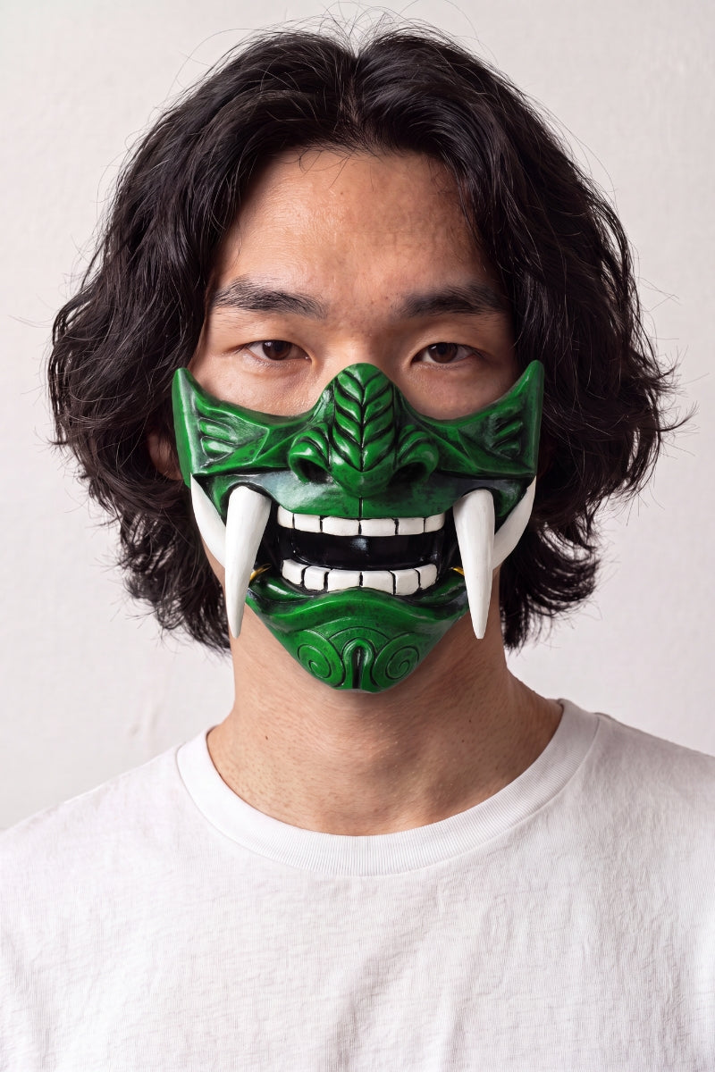 Grüne Mempō-Halbmaske von einem Model getragen — smaragdgrüner Gesichtsschutz mit gravierten Rippen, weißen Zähnen und vorstehenden Eckzähnen
