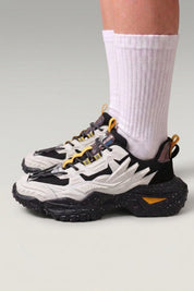 Chunky-Sneaker 'Shinshiro' in Weiß — gerippte Linien an den Seiten, gesprenkelte Sohle, am Fuß mit weißen Socken vor grauem Studiohintergrund