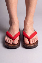 Japanische Flip Flops in uni rot, barfuß von vorn getragen — massive braune Holzsohle und gepolsterter Riemen zwischen den Zehen