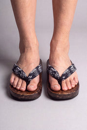Japanische Flip Flops in kleine blüten auf nachtblau, barfuß von vorn getragen — massive braune Holzsohle und gepolsterter Riemen zwischen den Zehen