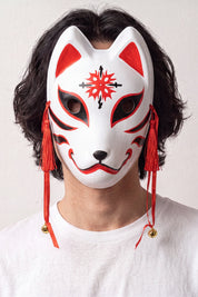 Kitsune-Maske mit Stern von einem Model vor hellem Hintergrund getragen — weißer Fuchs mit rotem Stern auf der Stirn, feinen Linien und roten Kordeln