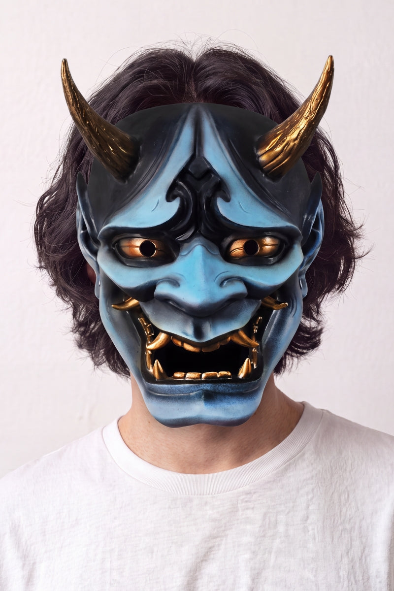Blaue Hannya-Maske von einem Model vor hellem Hintergrund getragen — blauer Dämon mit goldenen Hörnern, gerunzelten Brauen und offenem Mund voller Fangzähne