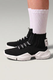 High-Top-Sneaker 'Kashiwa' in Schwarz — hoher Strickschaft ohne Schnürung, dicke Sohle, am Fuß mit weißen Socken vor grauem Studiohintergrund