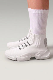 High-Top-Sneaker 'Kashiwa' in Weiß — hoher Strickschaft ohne Schnürung, dicke Sohle, am Fuß mit weißen Socken vor grauem Studiohintergrund