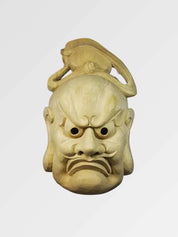 Bugaku-Maske von vorn vor einfarbig grauem Hintergrund — strenges Gesicht aus hellem Holz mit gebogener Kopfbedeckung und gerunzelten Brauen