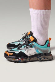 Chunky-Sneaker 'Hekinan' in Blau — transparente Sohle voller bunter Splitter, am Fuß mit weißen Socken vor grauem Studiohintergrund