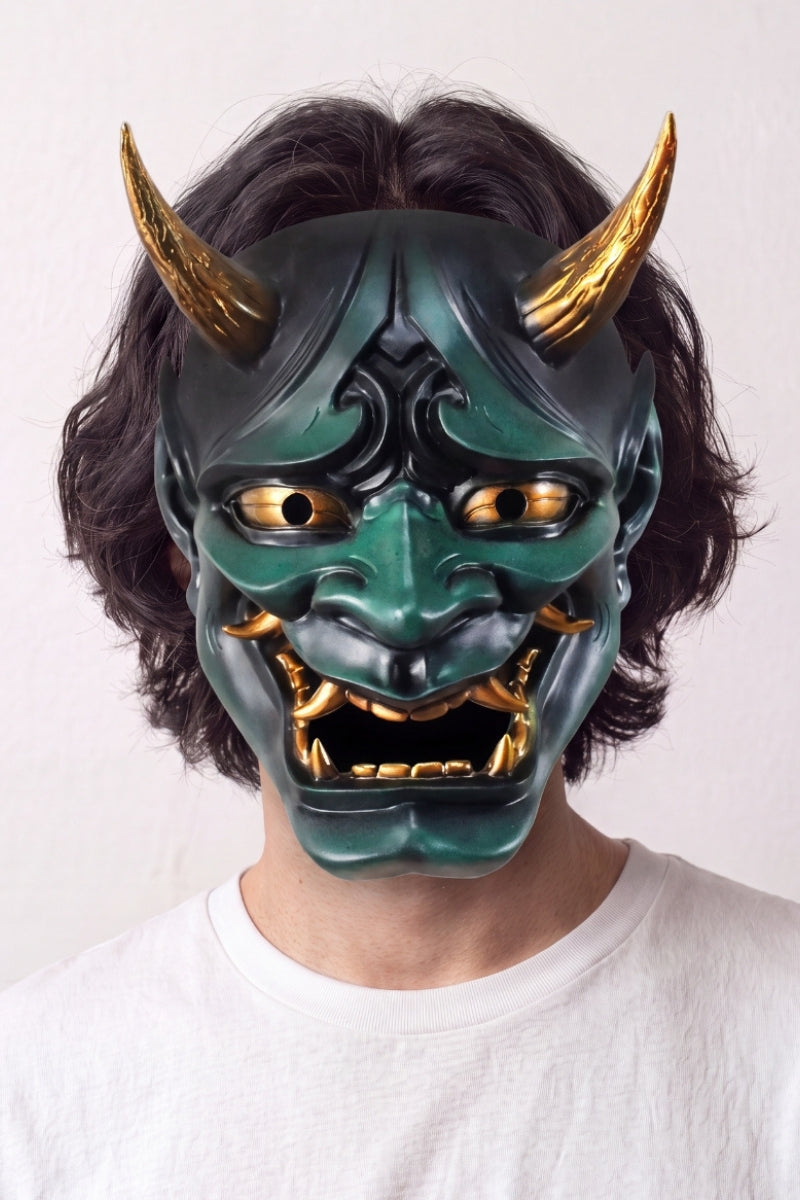Grüne Hannya-Maske von einem Model vor hellem Hintergrund getragen — grüner Dämon mit goldenen Hörnern, hervortretenden Augen und gefletschten Zähnen