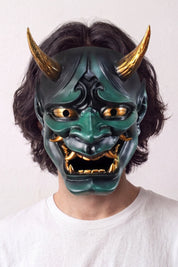 Grüne Hannya-Maske von einem Model vor hellem Hintergrund getragen — grüner Dämon mit goldenen Hörnern, hervortretenden Augen und gefletschten Zähnen
