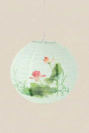 Japanische Laterne in Lotusblüte — wassergrüne Papierkugellaterne mit rosa Lotusblüte und breiten Blättern, an einer Schnur vor beigem Hintergrund
