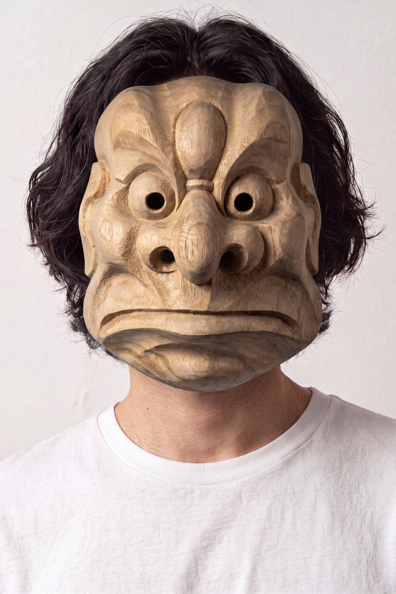 Karasu-Tengu-Maske von einem Model vor hellem Hintergrund getragen — geschnitzter Krähen-Tengu mit markantem Schnabel, großen runden Augen und gerippter Stirn