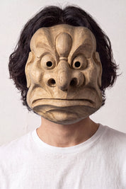 Karasu-Tengu-Maske von einem Model vor hellem Hintergrund getragen — geschnitzter Krähen-Tengu mit markantem Schnabel, großen runden Augen und gerippter Stirn