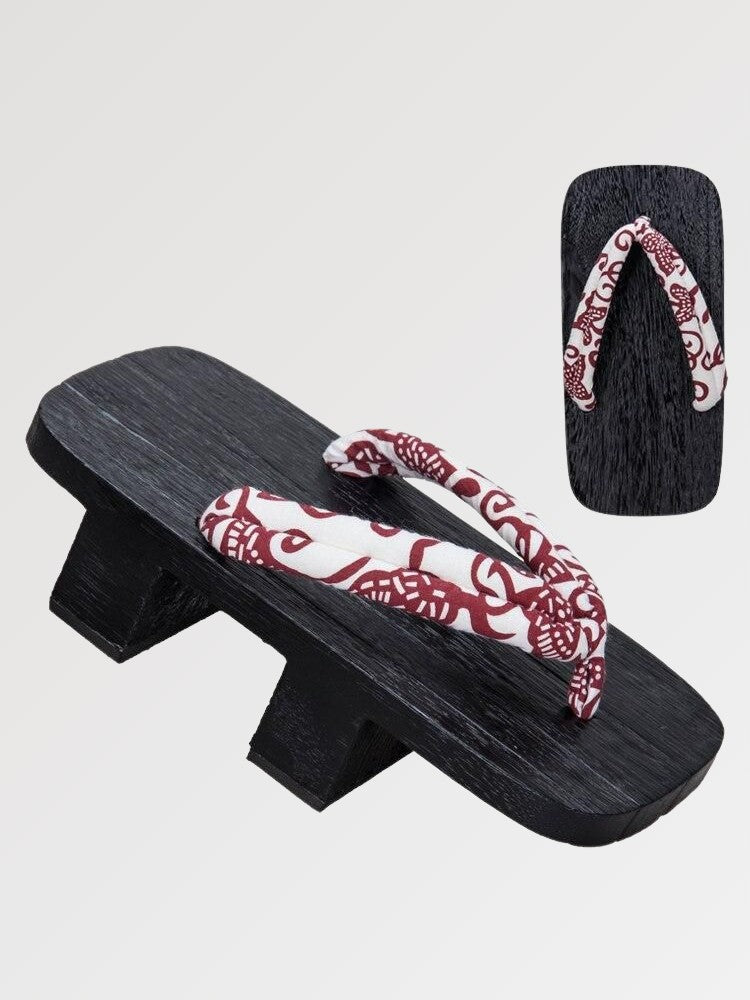 Paar Geta 'Aomori' schräg von vorn — Sockel aus schwarz gebeiztem Holz mit zwei Stegen, rot-weißer Riemen mit Paisleymuster, Unterseite sichtbar