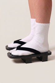 Japanischer Geta 'Hekinan' mit weißen Tabi-Socken von der Seite getragen — Plattform aus schwarz gebeiztem Holz, matt schwarzer Riemen passend zum Sockel