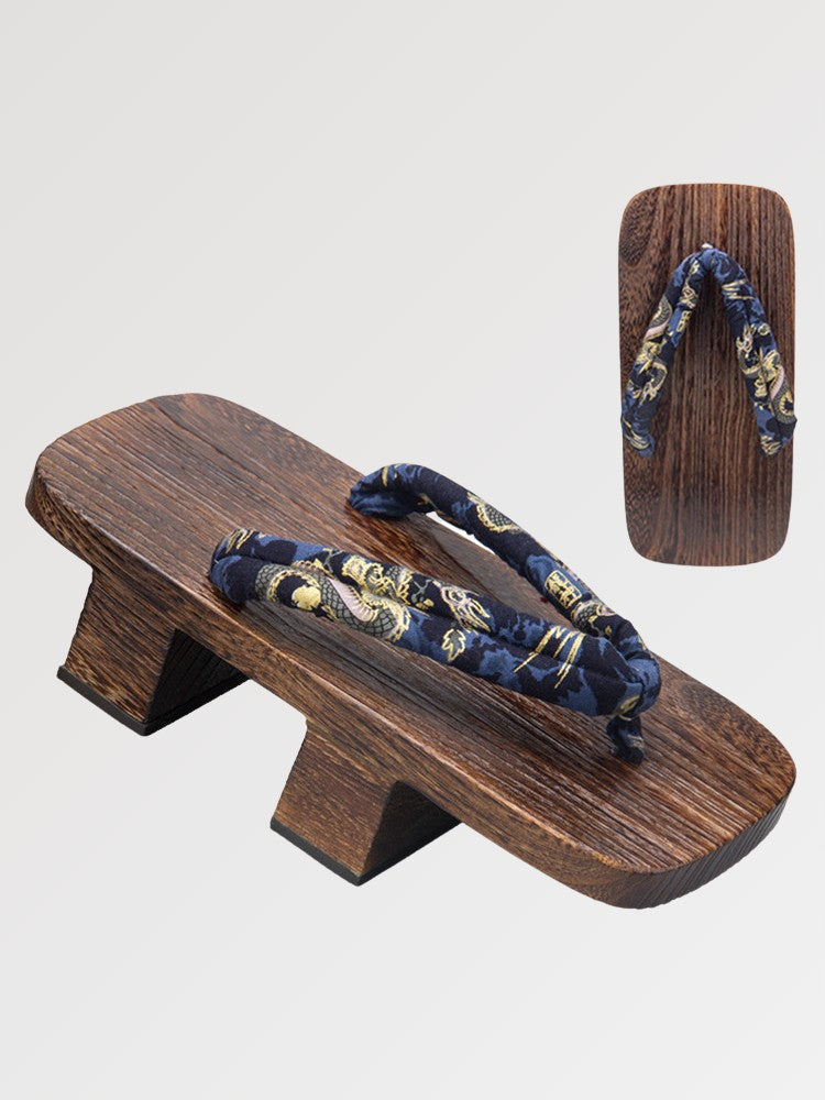 Paar Geta 'Inuyama' schräg von vorn — Sockel aus dunklem Holz mit zwei Stegen, nachtblauer Riemen mit goldenem Blumenmuster, Unterseite sichtbar