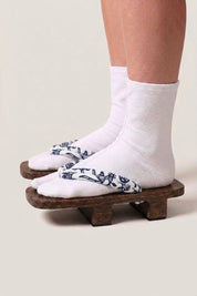 Japanischer Geta 'Okayama' mit weißen Tabi-Socken von der Seite getragen — Plattform aus braunem Holz, weißer Riemen mit nachtblauem Blumenmuster