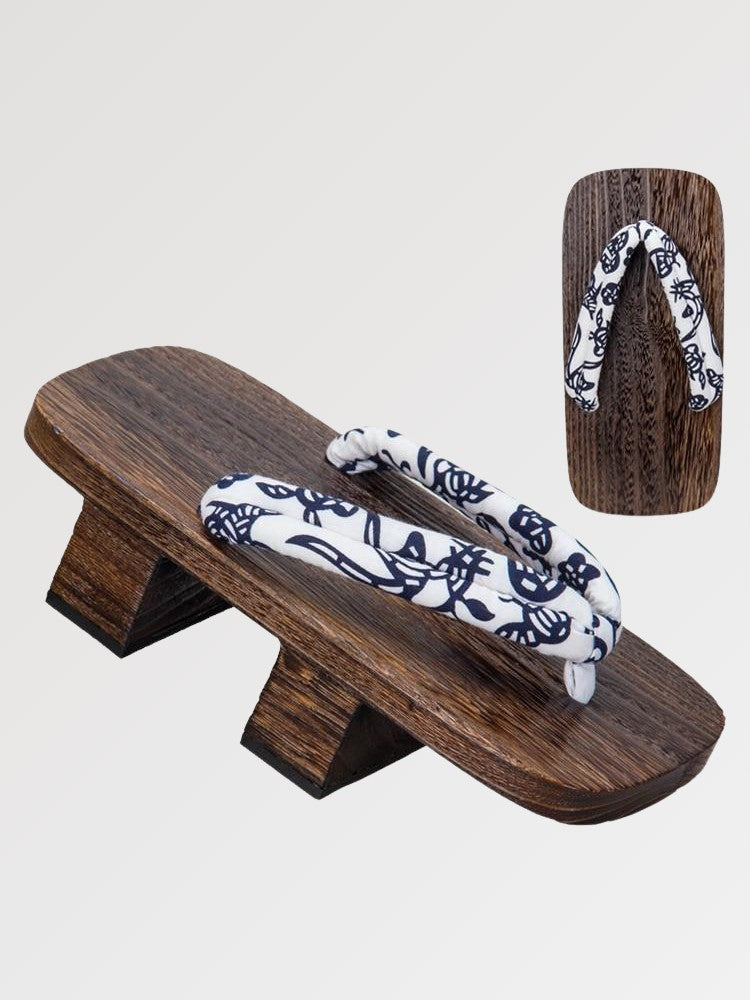 Paar Geta 'Okayama' schräg von vorn — Sockel aus braunem Holz mit zwei Stegen, weißer Riemen mit nachtblauem Blumenmuster, Unterseite sichtbar