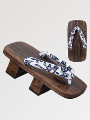 Paar Geta 'Okayama' schräg von vorn — Sockel aus braunem Holz mit zwei Stegen, weißer Riemen mit nachtblauem Blumenmuster, Unterseite sichtbar