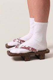 Japanischer Geta 'Shakori' mit weißen Tabi-Socken von der Seite getragen — Plattform aus dunklem Holz, tiefroter Riemen mit weißem Paisleymuster