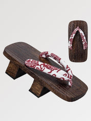 Paar Geta 'Shakori' schräg von vorn — Sockel aus dunklem Holz mit zwei Stegen, tiefroter Riemen mit weißem Paisleymuster, Unterseite sichtbar