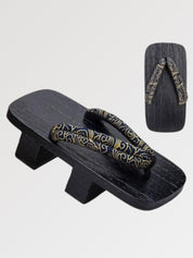 Paar Geta 'Tokoname' schräg von vorn — Sockel aus schwarz gebeiztem Holz mit zwei Stegen, dunkler Riemen mit goldenen Arabesken, Unterseite sichtbar