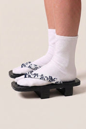 Japanischer Geta 'Utsomita' mit weißen Tabi-Socken von der Seite getragen — Plattform aus schwarz gebeiztem Holz, weißer Riemen mit nachtblauen Ranken