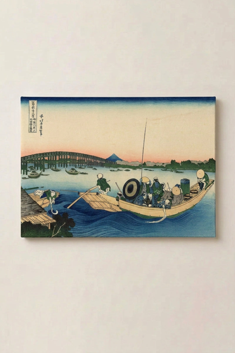 Japanischer Holzschnitt 'Ikebi' als Wandbild vor beiger Wand — beladenes Boot, das bei rosa Abendlicht unter einer Brücke hindurchgleitet, fern der Fuji