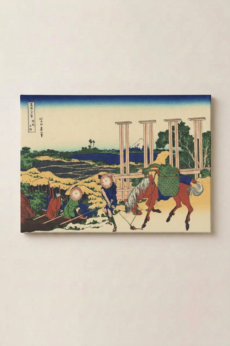 Japanischer Holzschnitt 'Umakishi' als gerahmtes Wandbild vor beiger Wand — von Pferdeknechten geführte Pferde vor einem Holzgerüst, im Mittelgrund der Fuji