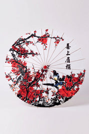 Japanischer Wagasa 'Kanji' von oben, flach geöffnet — weiße Bespannung mit rot-schwarzem Pflaumenzweig und Kalligrafie, Streben strahlen von der Nabe aus