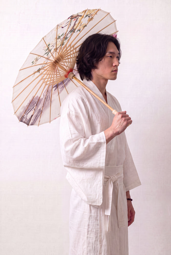 Japanischer Wagasa 'No-Kodai' geöffnet, von einem Model im weißen Kimono gehalten — cremefarbene Bespannung mit rosa blühendem Zweig auf freiem Grund