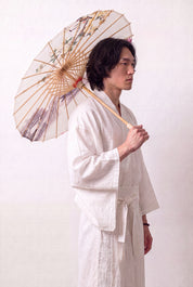 Japanischer Wagasa 'No-Kodai' geöffnet, von einem Model im weißen Kimono gehalten — cremefarbene Bespannung mit rosa blühendem Zweig auf freiem Grund