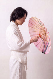Japanischer Wagasa 'Sakura Fleuri' von oben, flach geöffnet — rosa Verlaufsbespannung mit dunklem Zweig und Kirschblüten, Streben strahlen von der Nabe aus