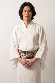 Obi-Gürtel 'Koshiko' über weißem Kimono von einem Model getragen — dunkler Brokat mit orangefarbenen und goldenen Chrysanthemen auf Blattgrund