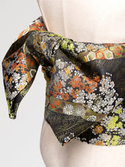 Nahaufnahme des Knotens des Obi-Gürtels 'Koshiko' an einer Schneiderbüste — dunkler Brokat mit orangefarbenen und goldenen Chrysanthemen auf Blattgrund