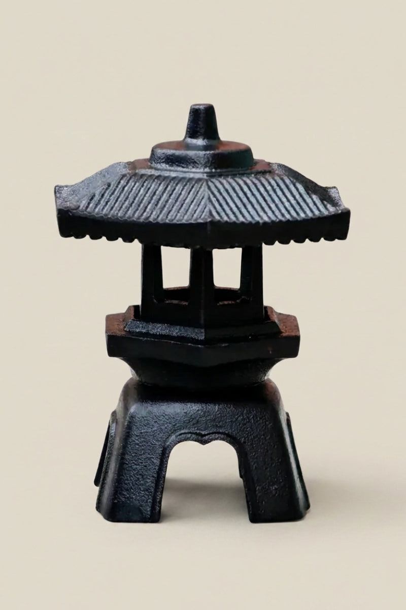 Japanische Laterne — kleine schwarze Gusseisenlaterne mit geripptem Sechseckdach und offenem Korpus auf vier Pfosten, Foto vor beigem Grund