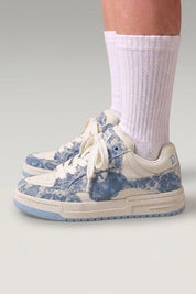 Low-Top-Sneaker 'Yuki' in Blau — schlichtes Canvas ohne sichtbare Nähte, flache Kontrastsohle, am Fuß mit weißen Socken vor grauem Studiohintergrund