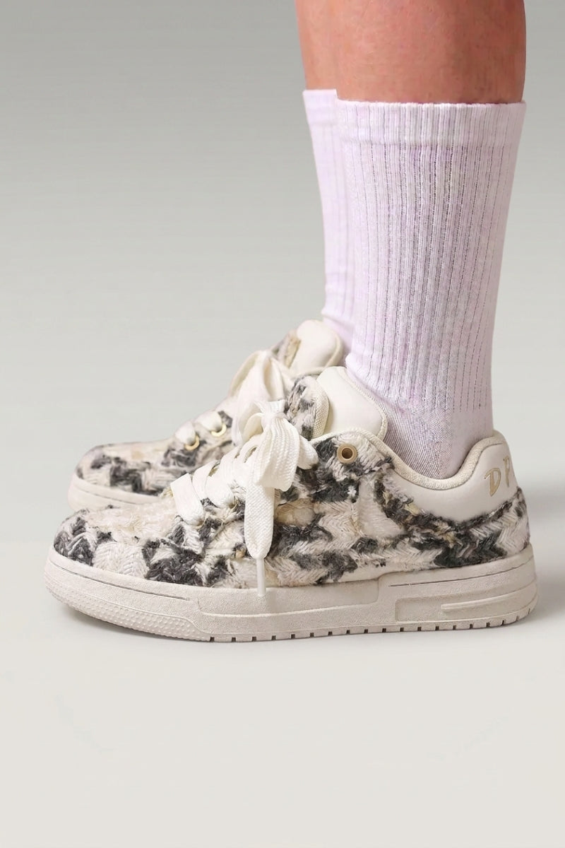 Low-Top-Sneaker 'Yuki' in Grau — schlichtes Canvas ohne sichtbare Nähte, flache Kontrastsohle, am Fuß mit weißen Socken vor grauem Studiohintergrund