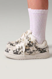 Low-Top-Sneaker 'Yuki' in Grau — schlichtes Canvas ohne sichtbare Nähte, flache Kontrastsohle, am Fuß mit weißen Socken vor grauem Studiohintergrund