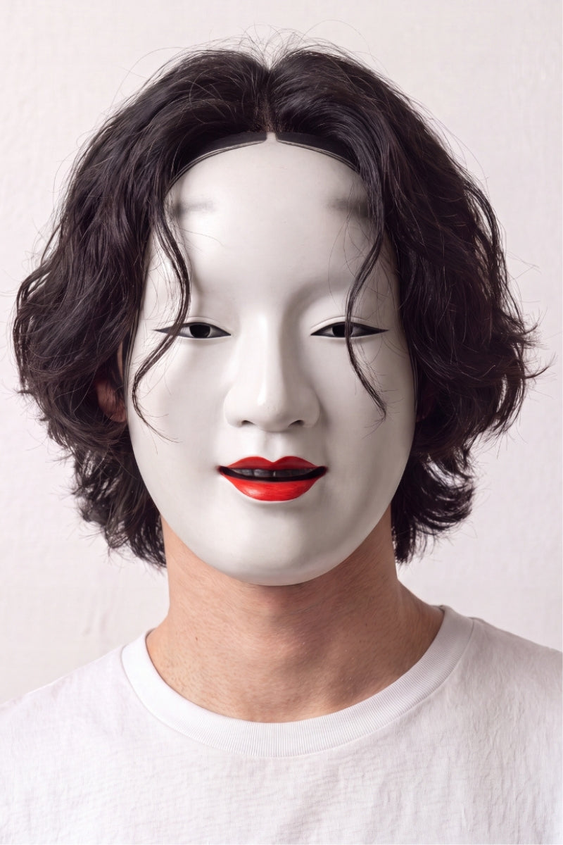 Noh-Maske von einem Model vor hellem Hintergrund getragen — weiß lackiertes Frauengesicht mit roten Lippen und hoch gemalten Brauen