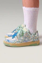 Low-Top-Sneaker 'Kasumi' in Grün — durchgehender Graffiti-Print, farblich abgestimmte Sohle, am Fuß mit weißen Socken vor grauem Studiohintergrund