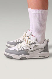 Low-Top-Sneaker 'Raijin' in Grau — übereinandergelegte Mesh-Panels, flache Rillensohle, am Fuß mit weißen Socken vor grauem Studiohintergrund