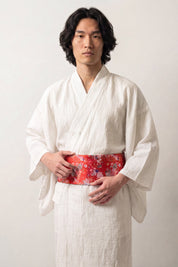 Obi-Gürtel 'Shochikubai' über weißem Kimono von einem Model getragen — leuchtend roter Grund voller kleiner weißer und bunter Blüten