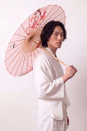 Japanischer Wagasa 'Sakura Classic' geöffnet, von einem Model im weißen Kimono gehalten — blassrosa Bespannung mit Vögeln und feinen blühenden Zweigen