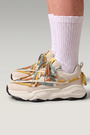 Chunky-Sneaker 'Fujioka' in Beige — doppelte bunte Schnürung, dicke cremefarbene Sohle, am Fuß mit weißen Socken vor grauem Studiohintergrund