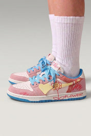 Low-Top-Sneaker 'Hanabi' in Rosa — bunte Patches, aufgenähte Blume an der Ferse, breite Schnürsenkel, am Fuß mit weißen Socken vor grauem Studiohintergrund
