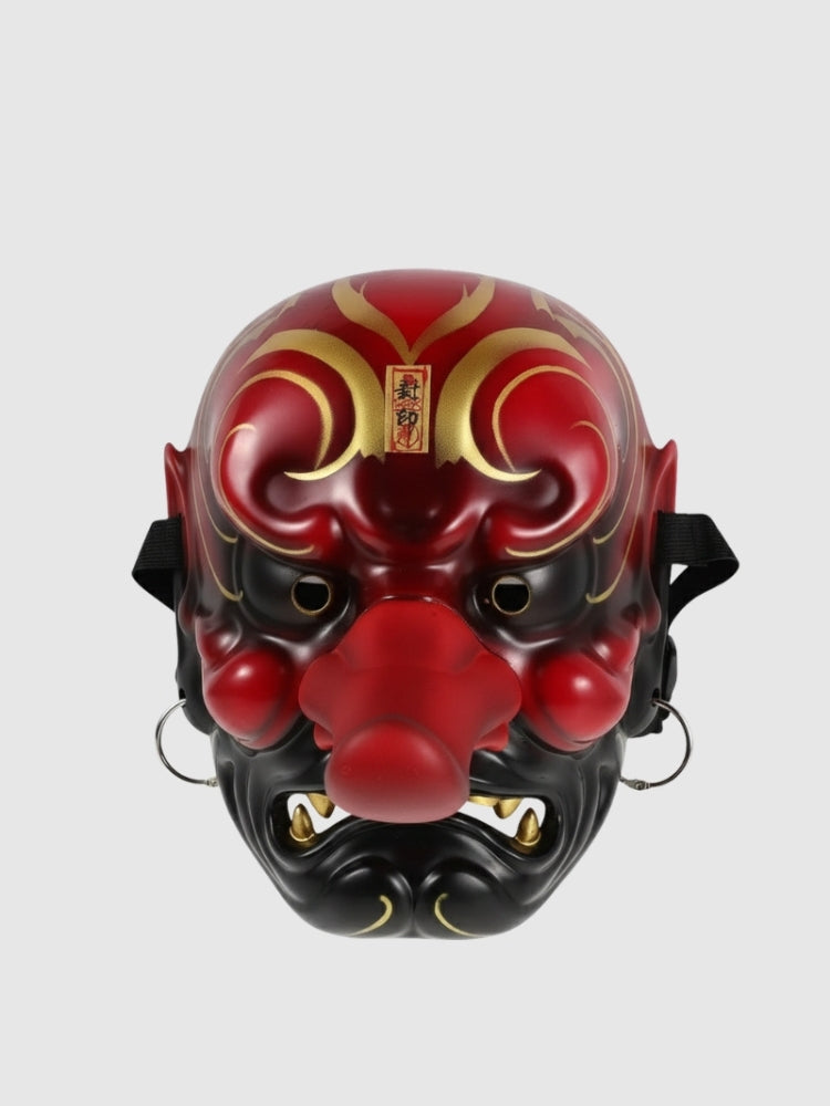 Tengu-Maske in Rot von vorn vor einfarbig grauem Hintergrund — lange markante Nase, goldene Brauenvoluten und weiße Fangzähne