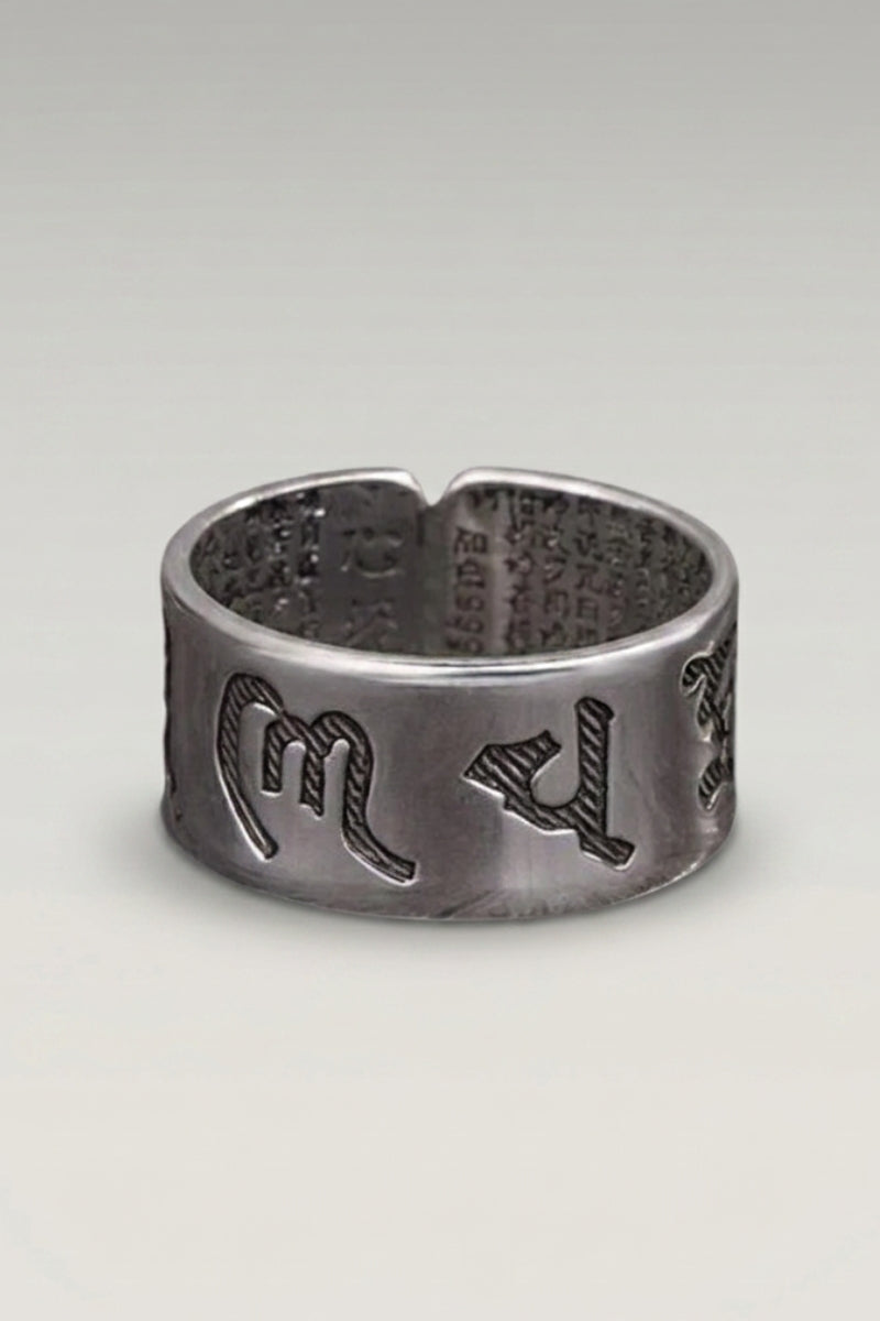 Ring 'Fujiwa' — breiter Ring mit roher dunkler Oberfläche und erhaben gearbeiteten Mantra-Zeichen, Produktfoto vor hellgrauem Hintergrund