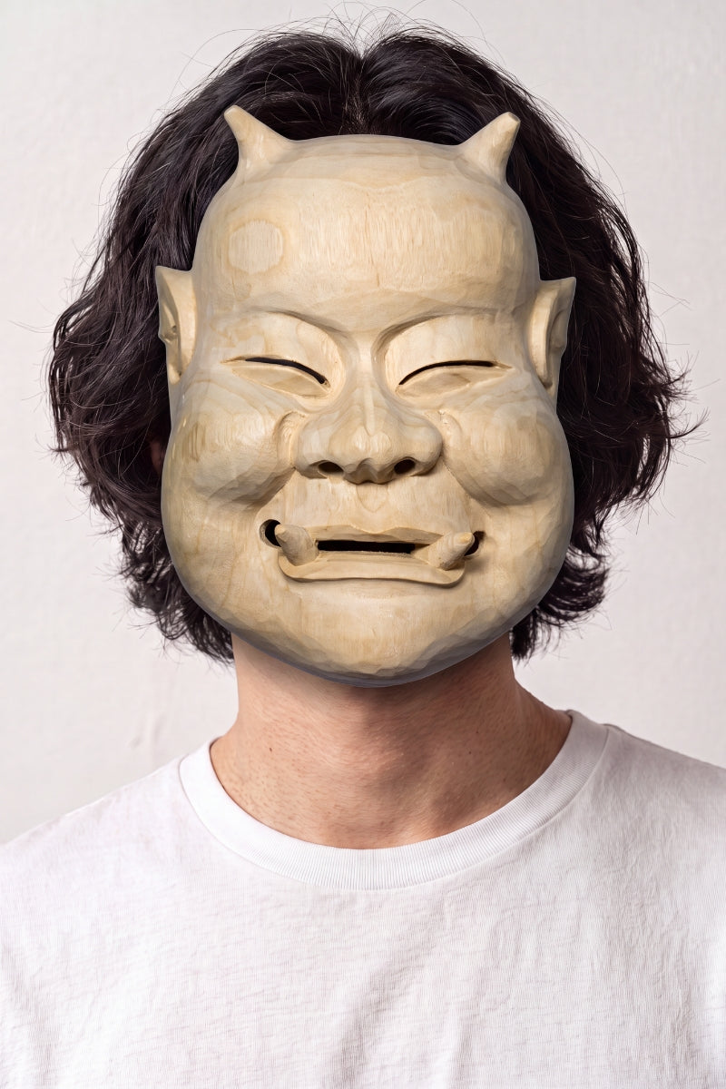 Beige Noh-Maske von einem Model vor hellem Hintergrund getragen — lächelndes altes Gesicht mit zusammengekniffenen Augen, sandfarben und schlicht modelliert